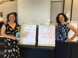 Authors Pam Berkman and Dorothy Hearst stand with large flip charts and a Pomeranian plush toy at a school visit